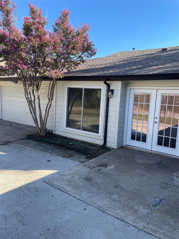 Exterior featuring light-colored horizontal siding, dual French doors with glass panes, a multi-car garage, and a large flowering crape myrtle tree