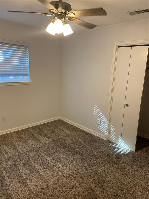 Neutral-toned carpeting, ceiling-mounted light fixture with a fan, and white bifold closet doors