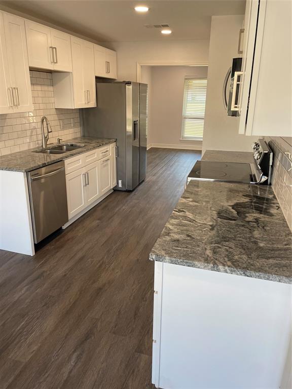 Kitchen featuring white shaker-style cabinetry, patterned stone countertops, stainless steel appliances, subway tile backsplash, and wood-finish flooring