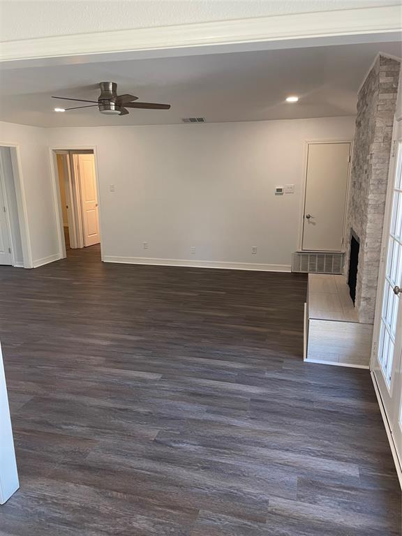 Open-concept area featuring wood-finish flooring, a floor-to-ceiling stone-clad fireplace, a raised stone hearth, and a ceiling fan
