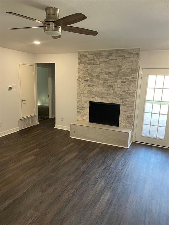 Fireplace featuring a floor-to-ceiling stacked stone surround, wood-finish flooring, a modern multi-blade ceiling fan, and a glass-paneled door