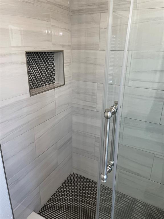 Walk-in shower featuring large-format horizontal tile walls, a built-in recessed tiled niche, black penny tile flooring, and a glass enclosure with a metallic pull handle