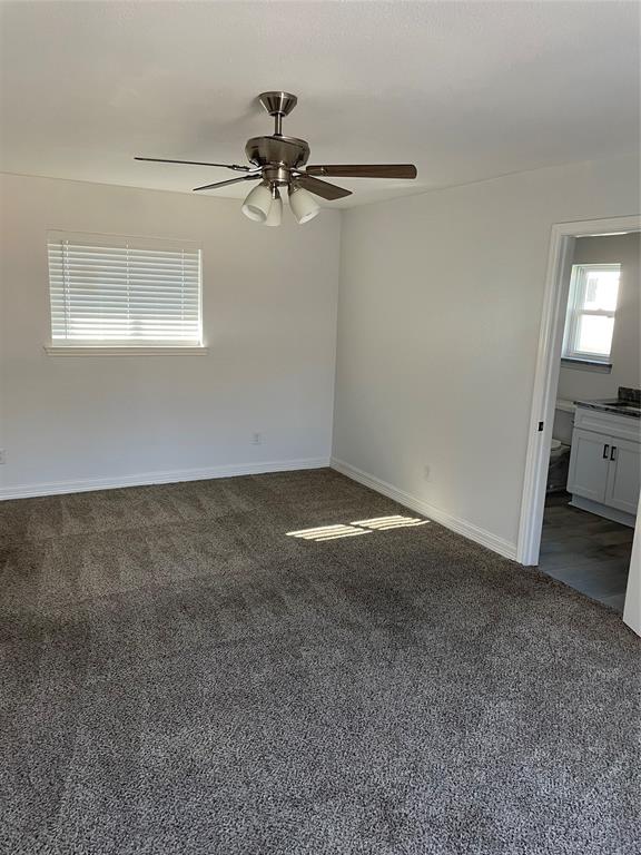Interior space featuring wall-to-wall carpeting, brushed nickel ceiling fan with integrated lighting, horizontal window blinds, and a built-in white vanity with stone-top surface