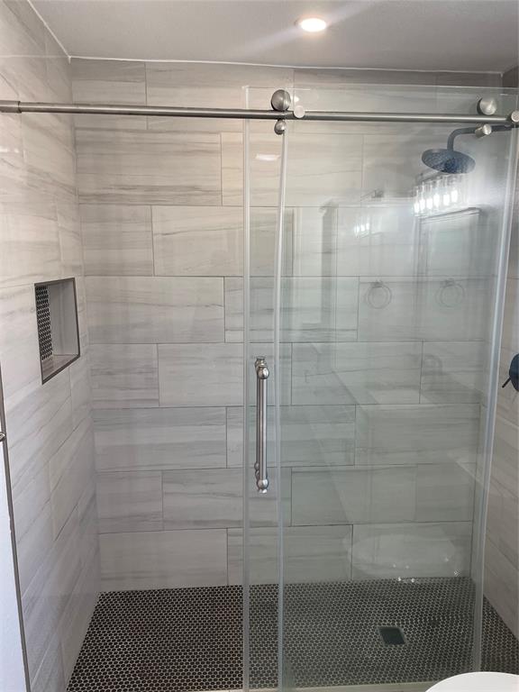Walk-in shower featuring large-format neutral wall tile, circular mosaic floor tile, brushed nickel sliding glass door hardware, a recessed wall niche, and a rain-style shower head