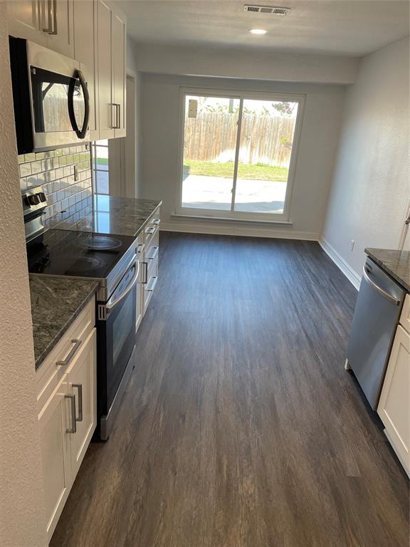 Kitchen featuring white shaker cabinetry, stone-finish countertops, subway tile backsplash, stainless steel appliances, and wood-finish flooring with sliding glass door access to the exterior