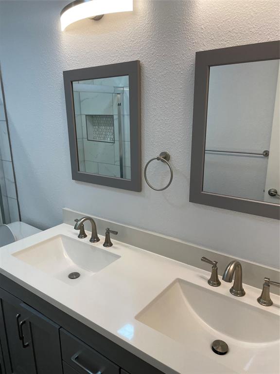 Double vanity featuring a light-toned countertop with integrated dual sinks, brushed nickel widespread faucets, framed mirrors, and a wall-mounted light fixture