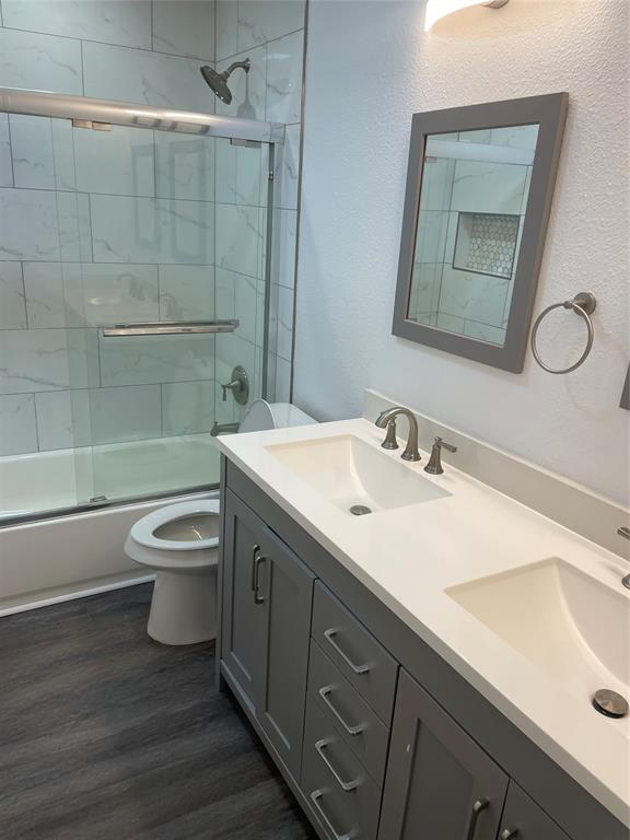 Double vanity featuring quartz countertops, undermount sinks, grey shaker-style cabinetry, and a shower-tub combination with tiled surround and glass sliding doors