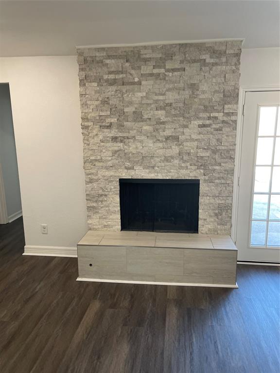 Fireplace with stacked stone veneer, raised hearth, and wood-finish flooring