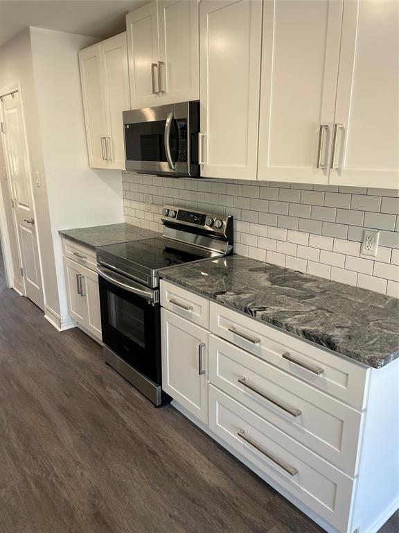 Kitchen featuring white Shaker-style cabinetry, dark stone countertops, stainless steel appliances, subway tile backsplash, and wood-finish flooring