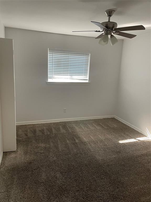Neutral-toned carpeting, ceiling fan with integrated lighting, window with horizontal blinds, and built-in closet cabinetry