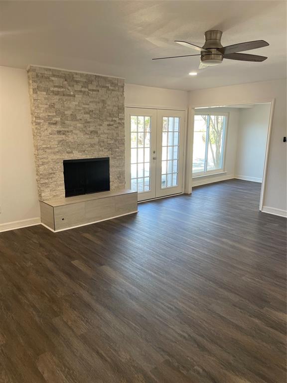 Stacked stone fireplace with a built-in hearth, wood-finish flooring, double glass-paneled doors, and a ceiling-mounted fan
