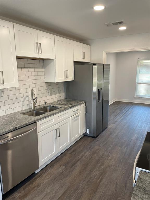 Kitchen featuring white shaker-style cabinetry, stone-patterned countertops, a subway tile backsplash, stainless steel appliances, and wood-finish flooring