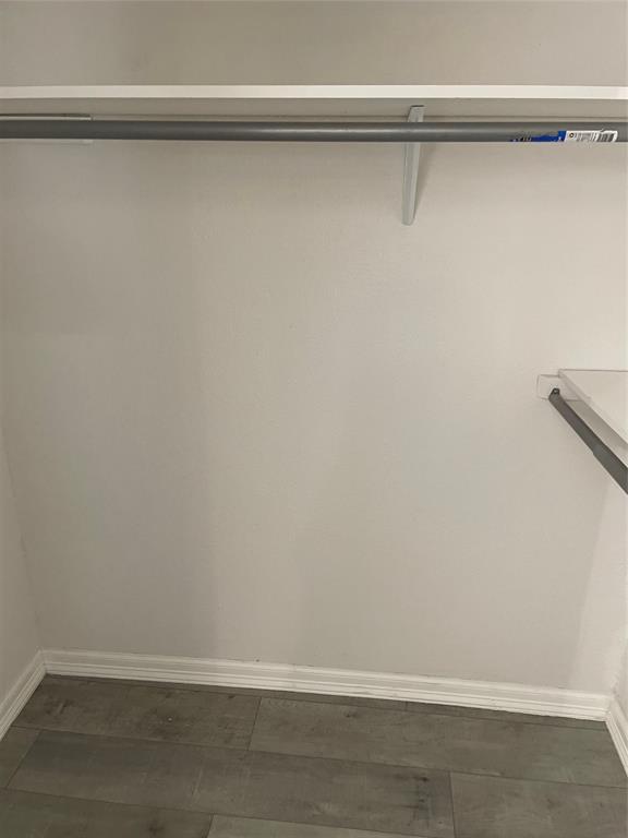 Storage space featuring upper shelving, a horizontal hanging rod, and wood-finish flooring