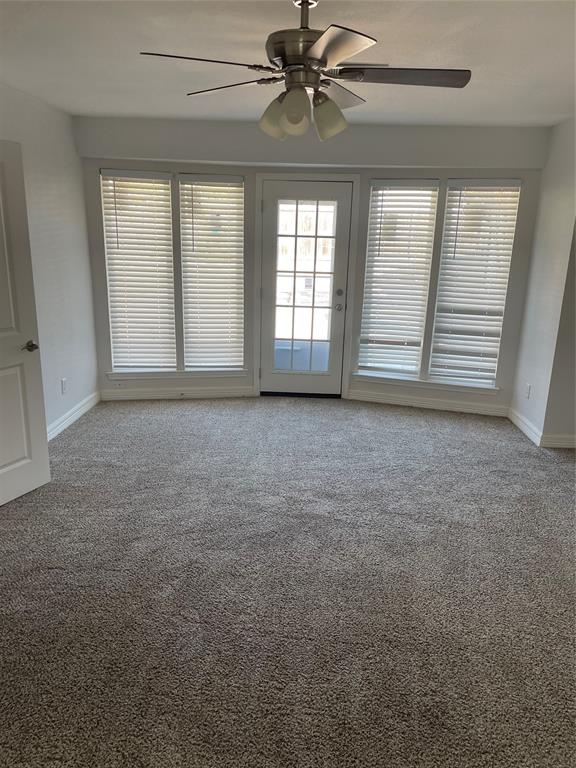Wall-to-wall carpeting, four large windows, glass-paneled exterior door, and a ceiling fan with integrated lighting