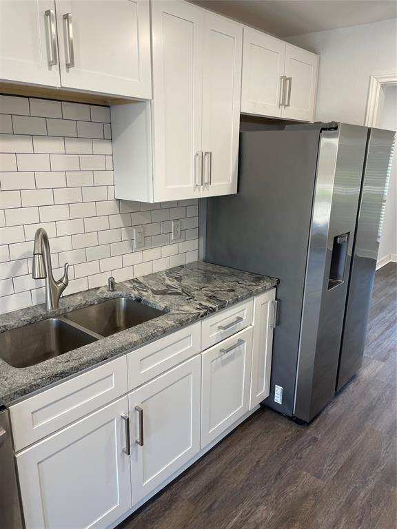 Kitchen featuring white shaker-style cabinetry, stone countertops, stainless steel dual-basin sink with arched faucet, subway tile backsplash, and wood-finish flooring
