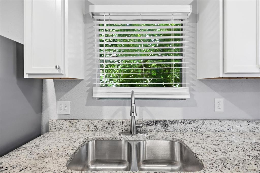 Double basin stainless steel sink with a high-arch pull-down faucet, light-toned stone-finish countertop, white cabinetry, and horizontal window blinds