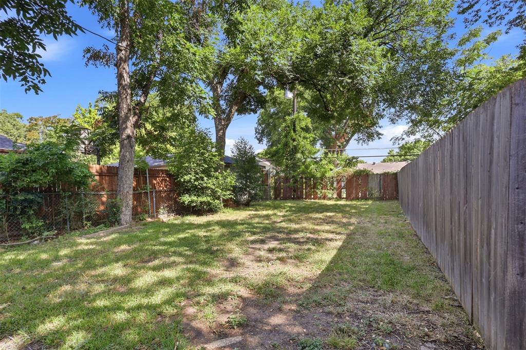 Rear yard featuring grass landscaping, mature trees, and wooden perimeter fencing