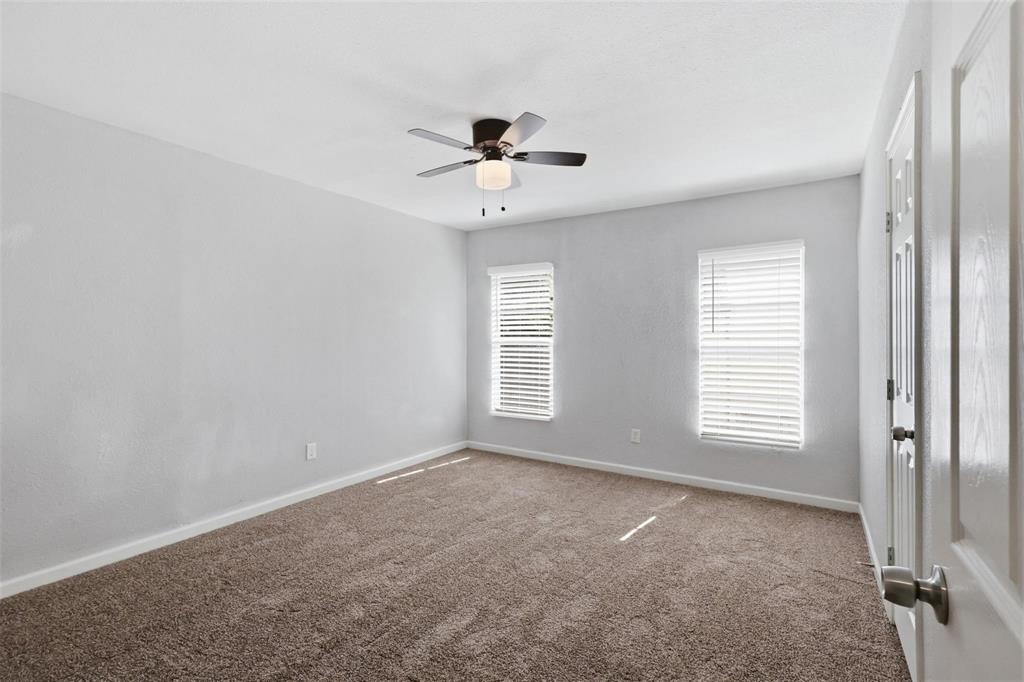 Neutral-toned interior space featuring carpeting, two windows with installed blinds, and a centrally mounted ceiling fan