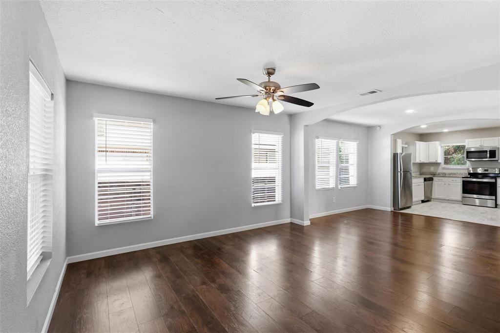 Wood-finish flooring, neutral wall tones, multi-light ceiling fan, multiple windows with integrated blinds, and arched architectural detailing Wood-finish flooring, neutral wall tones, multi-light ceiling fan, multiple windows with integrated blinds, and arched architectural detailing