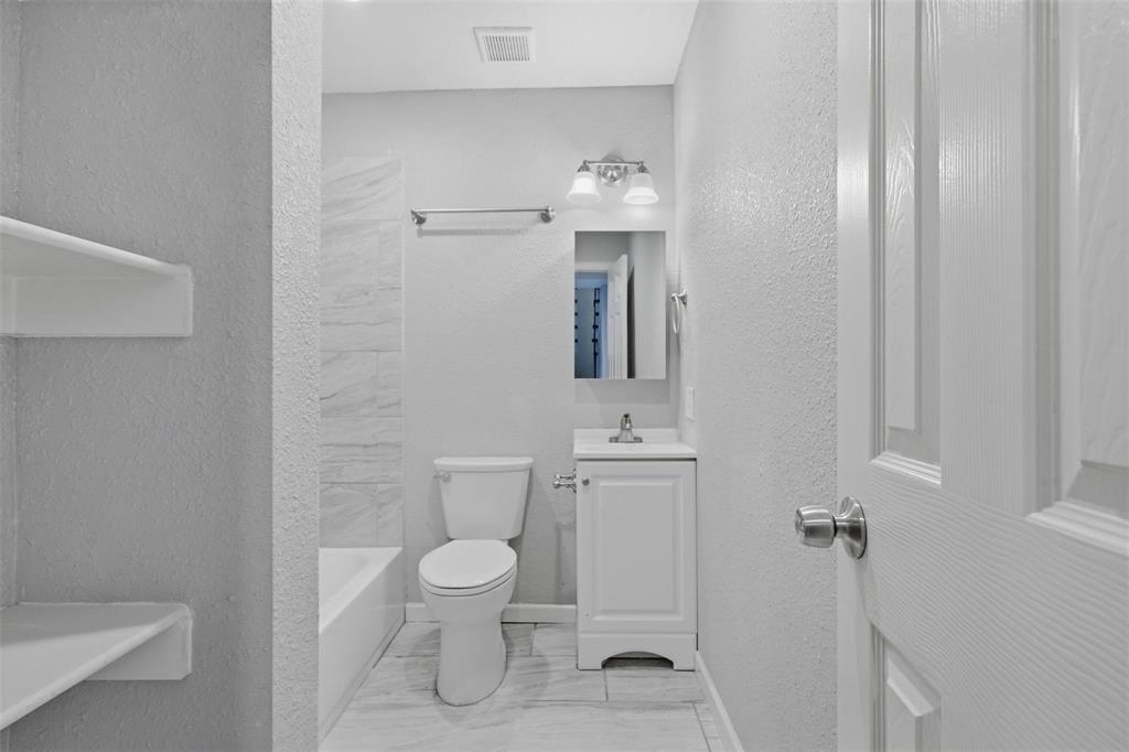 Full bathroom featuring a white vanity cabinet with a stone-top sink, tub-shower combination with light-toned wall tile, built-in recessed shelving, and a dual-light fixture