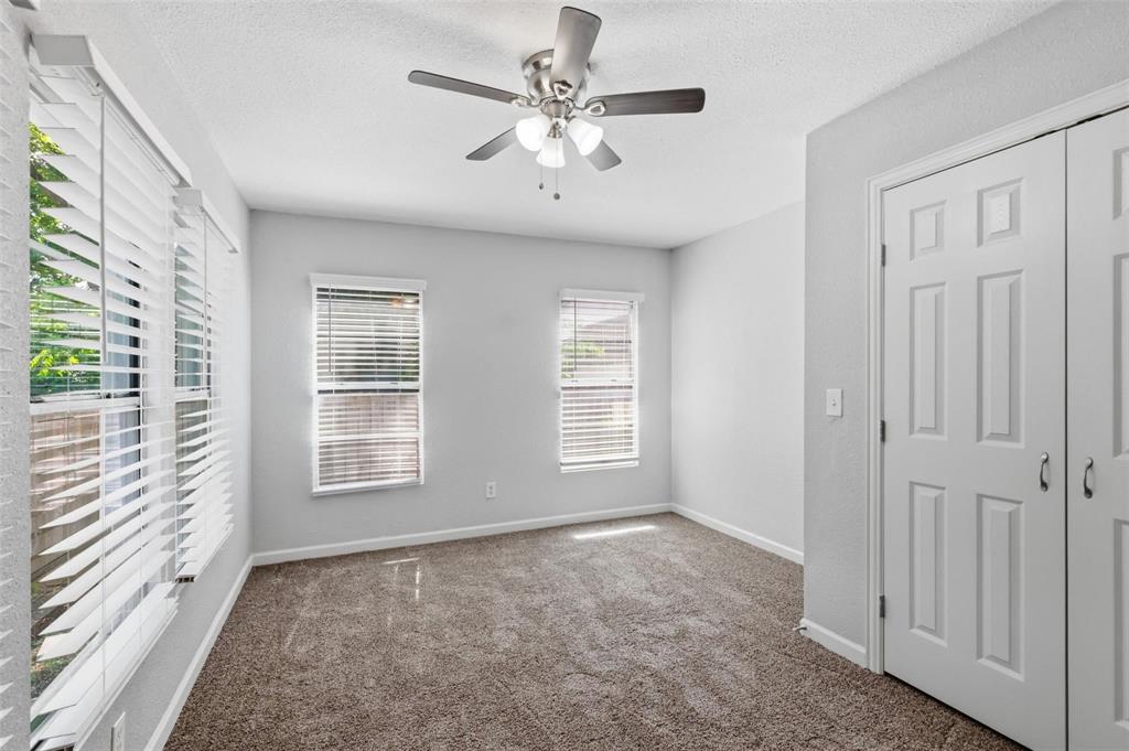 Neutral-toned room featuring carpeted flooring, two double-panel windows with adjustable horizontal blinds, a ceiling fan with integrated light fixture, and a white paneled closet door