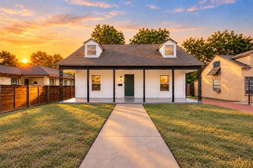 Exterior featuring white siding, a covered front porch with iron support columns, dual roof dormers, and a concrete walkway Exterior featuring white siding, a covered front porch with iron support columns, dual roof dormers, and a concrete walkway