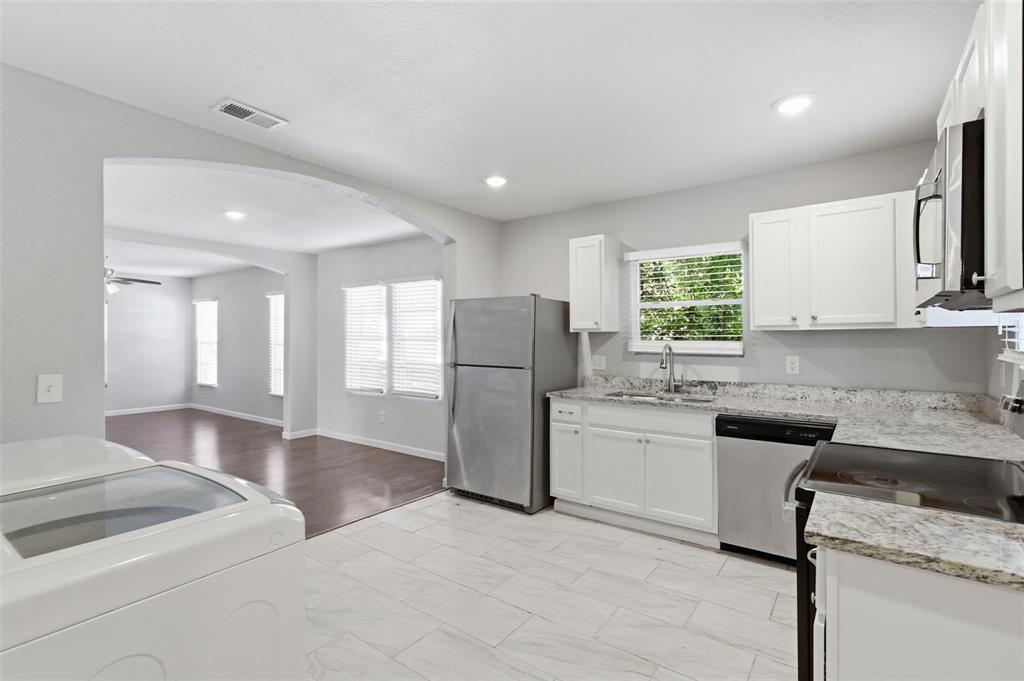 Kitchen featuring white cabinetry, stone-finish countertops, stainless steel appliances, and large-format tile flooring, highlighted by an arched architectural opening Kitchen featuring white cabinetry, stone-finish countertops, stainless steel appliances, and large-format tile flooring, highlighted by an arched architectural opening