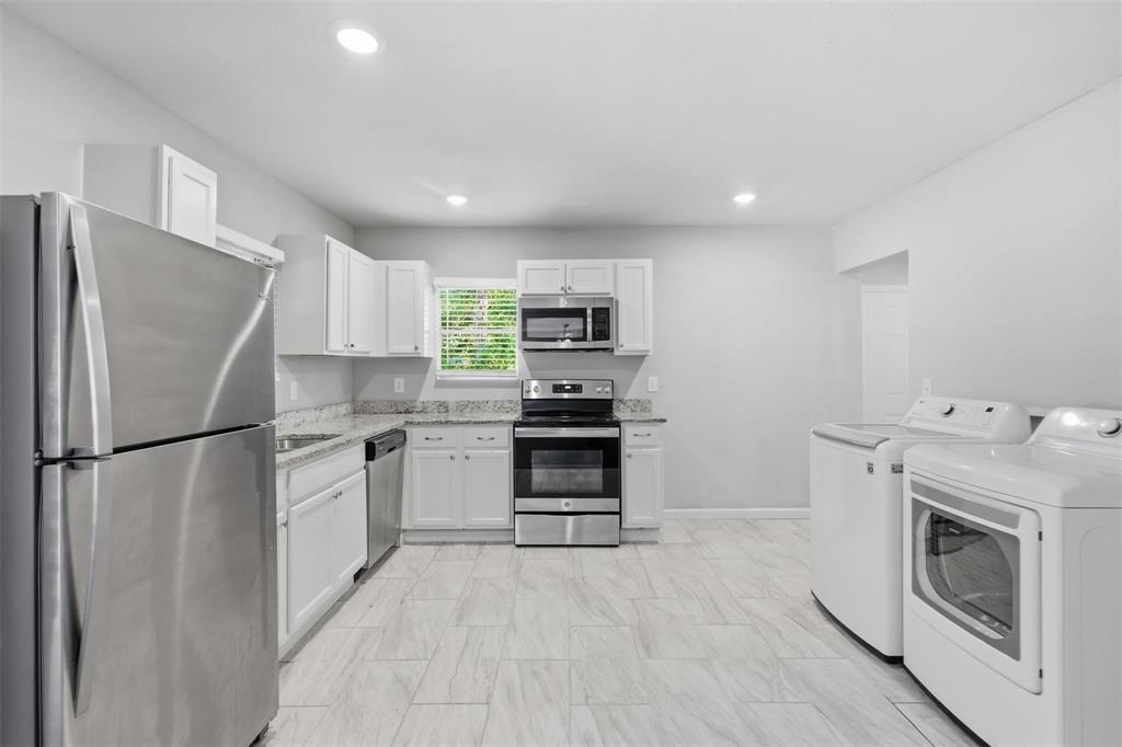 Kitchen featuring white shaker-style cabinetry, stone-finish countertops, stainless steel appliances, and tile flooring Kitchen featuring white shaker-style cabinetry, stone-finish countertops, stainless steel appliances, and tile flooring