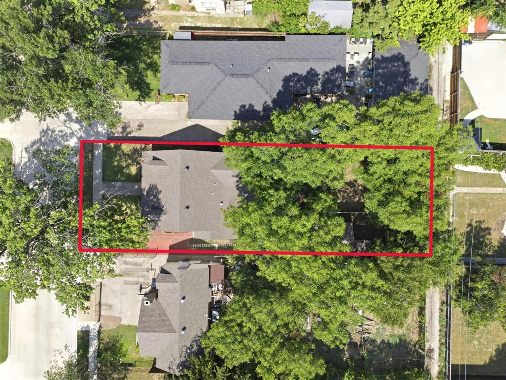 Aerial perspective of a residential lot featuring mature tree canopy, grass lawn, and paved walkway