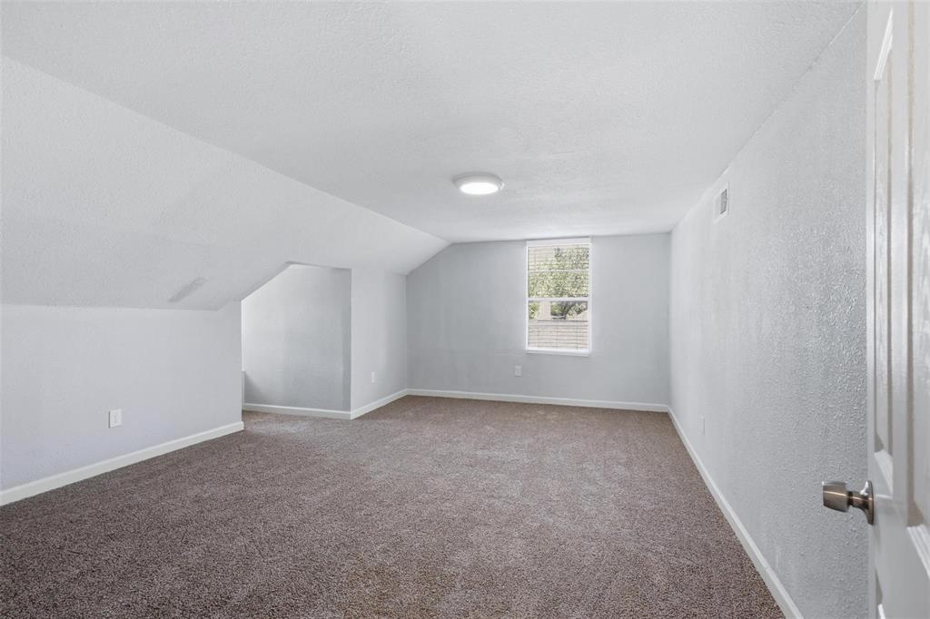 Interior room featuring neutral wall-to-wall carpeting, angled ceiling architecture, a single-pane window, and a flush-mount ceiling light fixture