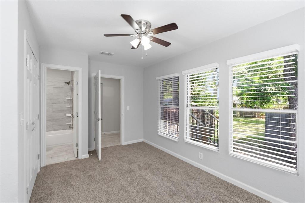 Neutral-toned room featuring wall-to-wall carpeting, a multi-light ceiling fan, and three large windows with horizontal blinds