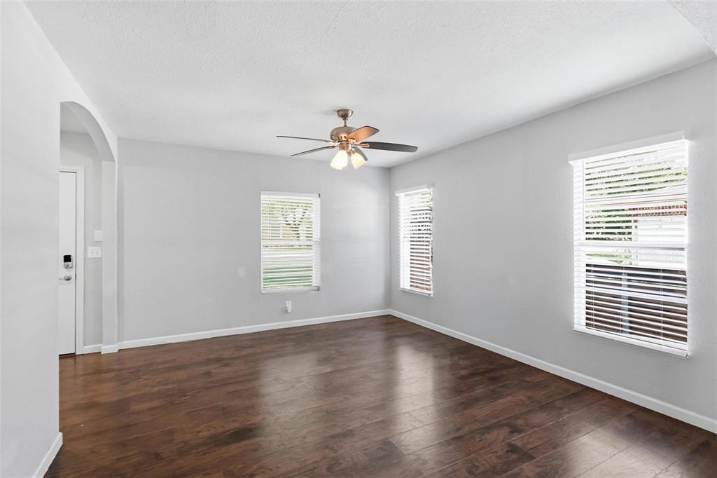 Neutral interior space featuring wood-finish flooring, white walls, multiple windows with horizontal blinds, and a central ceiling fan with integrated lighting Neutral interior space featuring wood-finish flooring, white walls, multiple windows with horizontal blinds, and a central ceiling fan with integrated lighting