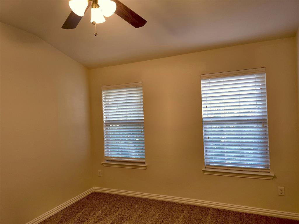 Room with neutral wall color, dual windows featuring horizontal blinds, and a ceiling fan