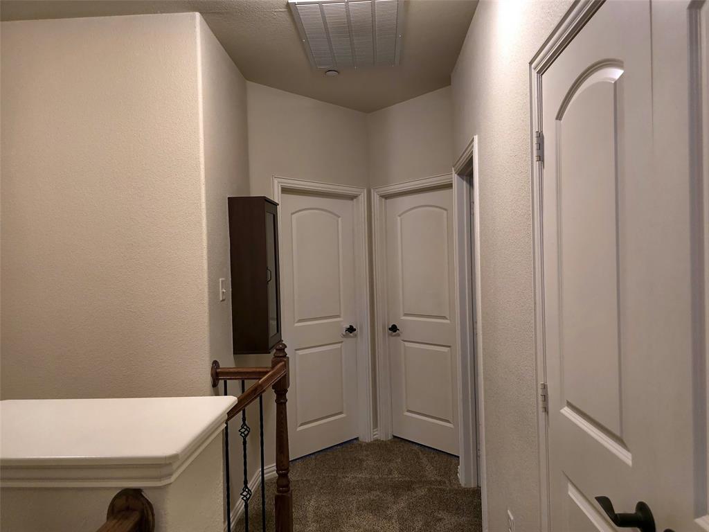 Hallway featuring three arched-panel interior doors, neutral wall-to-wall carpeting, and a wooden handrail with vertical metal spindles