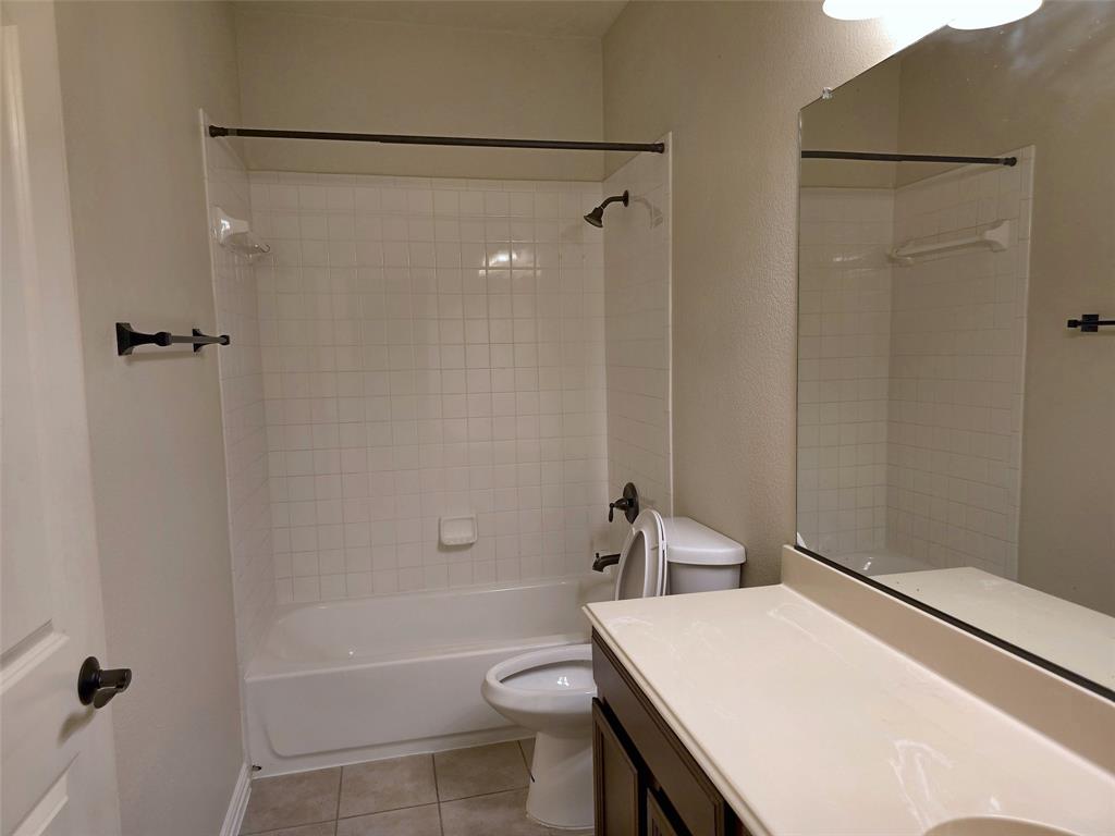 Full-width vanity with countertop, wall-mounted mirror, tub-shower combination with tile surround, and neutral floor tile