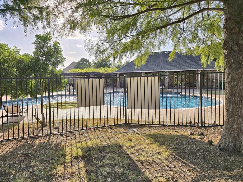 Swimming pool with a paved deck, enclosed by a black metal fence, featuring a pergola and brick-exterior structures