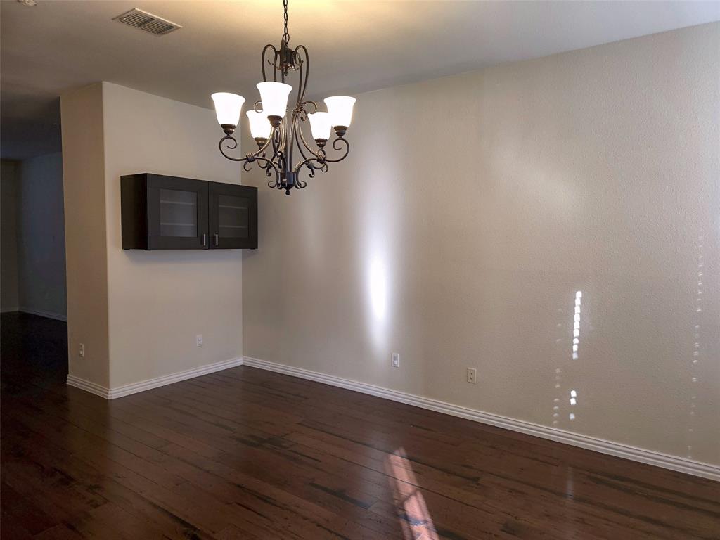 Wood-finish flooring, dark-toned wall-mounted cabinetry with glass-panel doors, and an ornate metal chandelier featuring five frosted-glass shades
