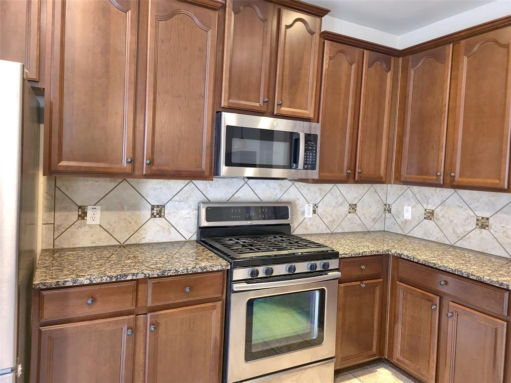 Kitchen featuring stained wood cabinetry, stone countertops, stainless steel gas range, over-the-range microwave, and a tile backsplash with decorative accents