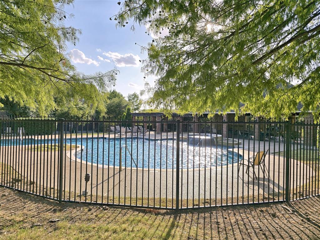 Swimming pool featuring a concrete surround, elevated spa, wrought-iron perimeter fencing, and an expansive covered pavilion