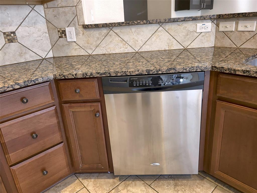 Stained wood cabinetry, stone-finish countertops, stainless steel dishwasher, and diagonal-pattern tile backsplash