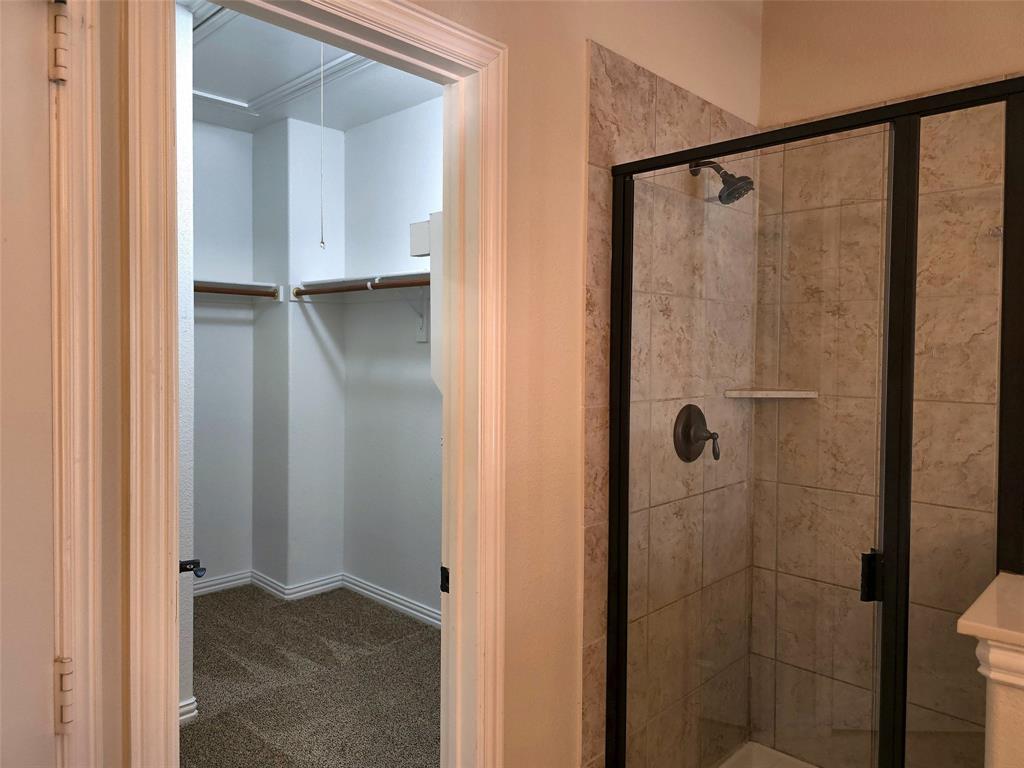 Walk-in closet featuring integrated shelving and carpeting, accompanied by a shower enclosure with stone-tile surround, metal-framed glass door, and oil-rubbed bronze fixtures