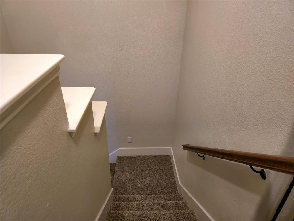 Staircase featuring neutral-toned carpeting, painted wall caps, and a wall-mounted wooden handrail with metal hardware