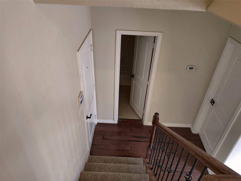 Staircase featuring a wooden handrail with metal balusters, carpeted steps, wood-finish flooring, and white paneled doors Staircase featuring a wooden handrail with metal balusters, carpeted steps, wood-finish flooring, and white paneled doors