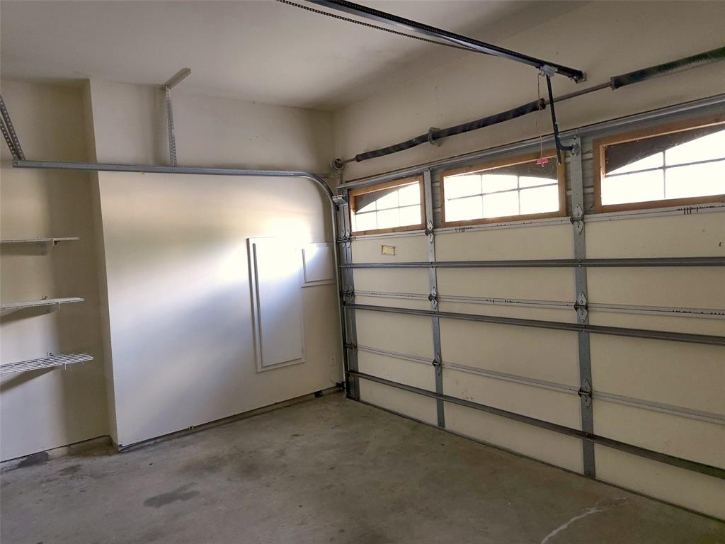 Garage interior featuring a sectional paneled door with integrated transom windows, exposed ceiling-mounted door hardware, and built-in wall shelving