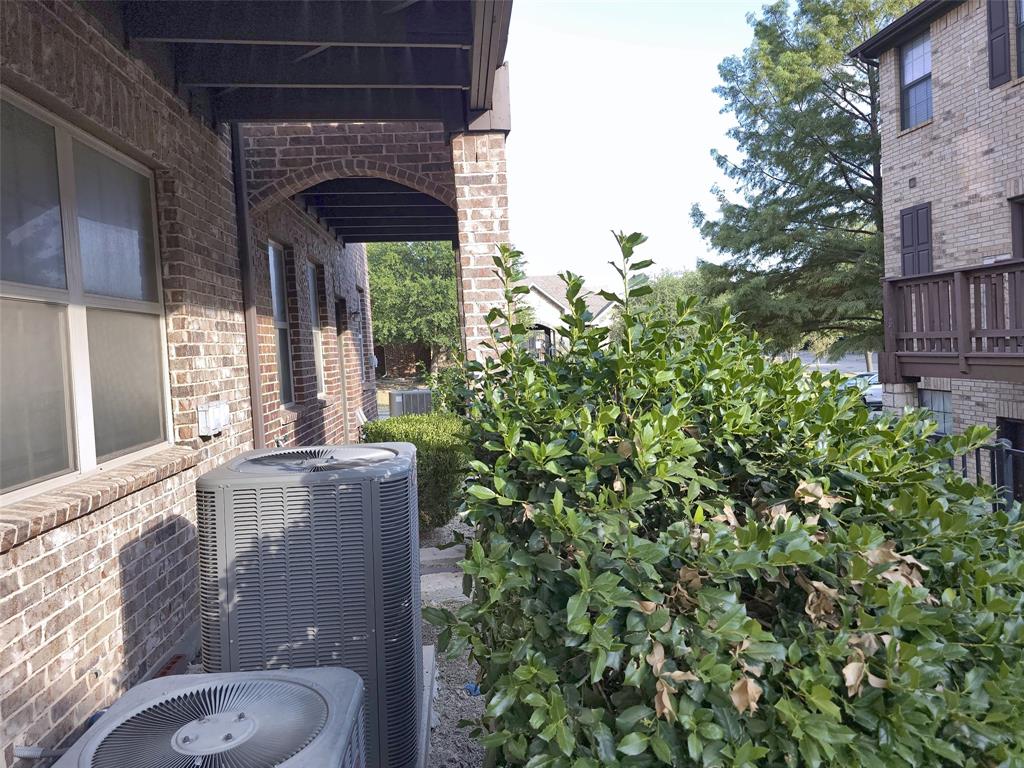 Exterior brick facade featuring arched architectural detailing, covered outdoor structure, and mature landscaping