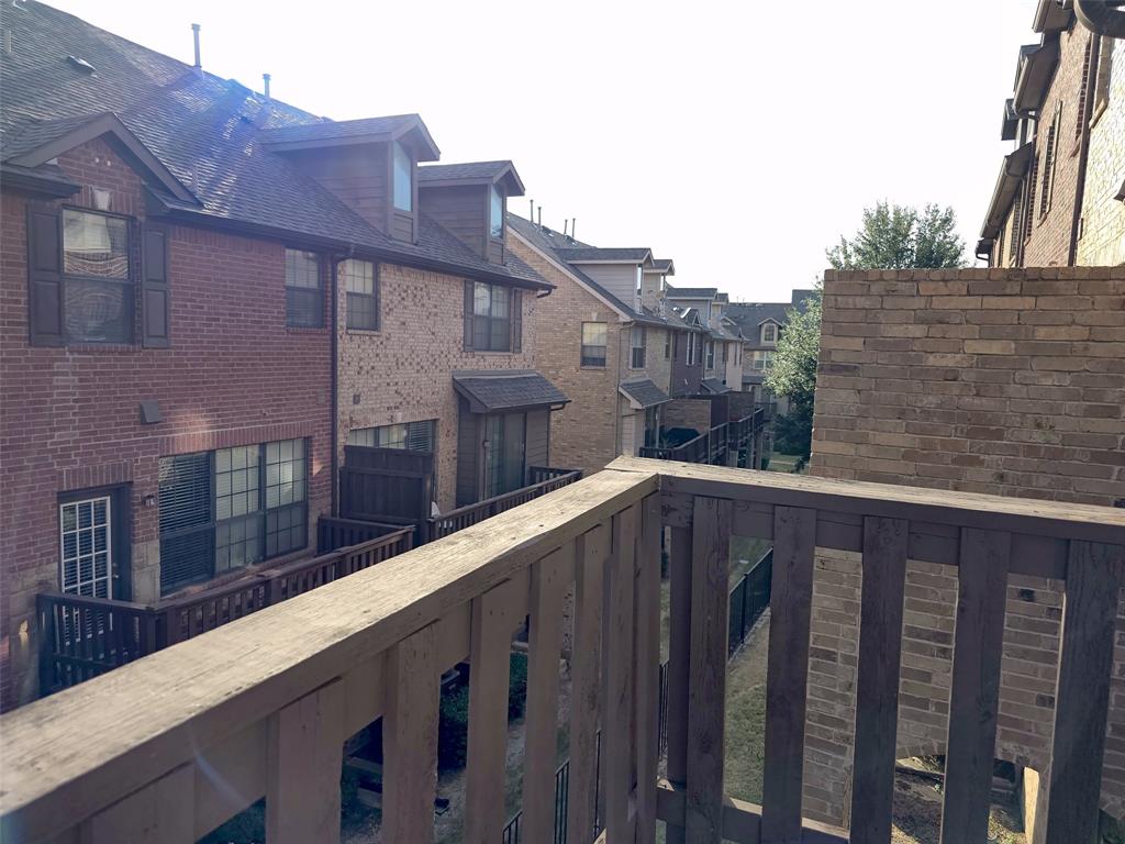 Elevated deck with wooden railings, multi-story brick exterior, and roof dormers