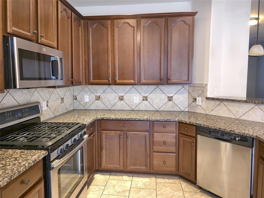 Kitchen featuring stained wood cabinetry, stone-finish countertops, stainless steel appliances, a diamond-pattern tile backsplash with decorative accents, and tiled flooring