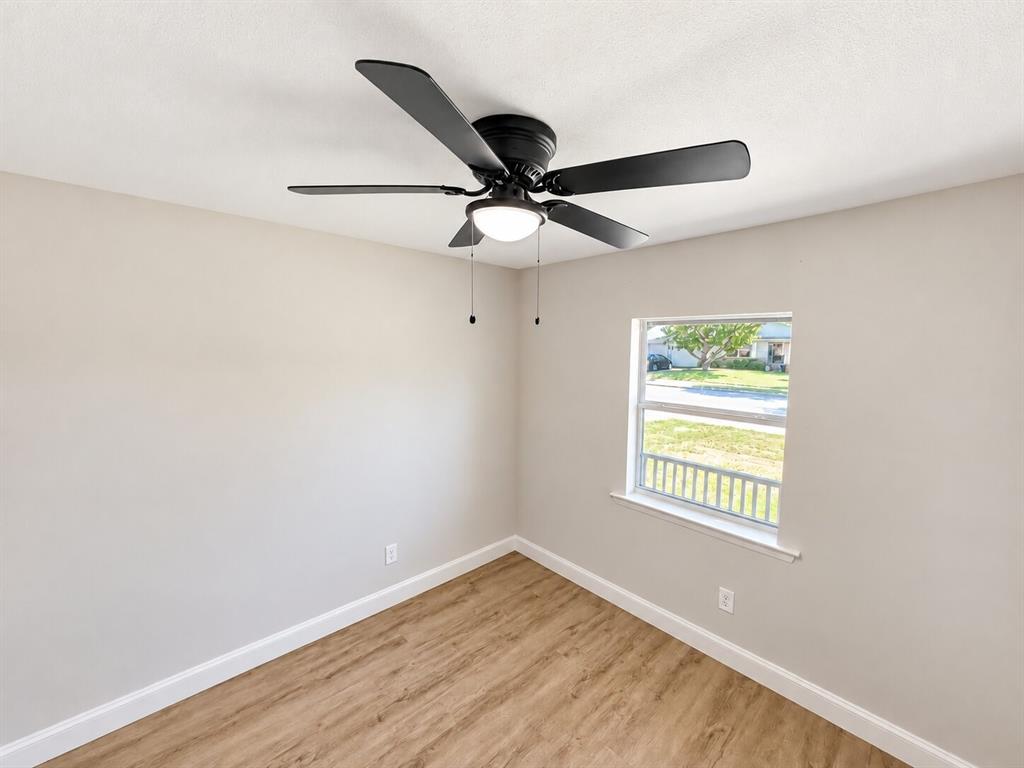 Neutral wall finish, wood-finish flooring, and black matte five-blade ceiling fan with integrated dome lighting and single-pane window