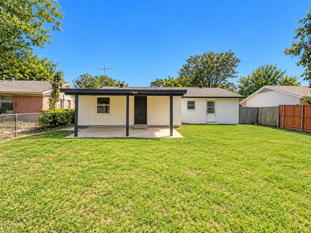 Rear exterior featuring a covered concrete patio, light-colored siding, and a fenced backyard with lawn