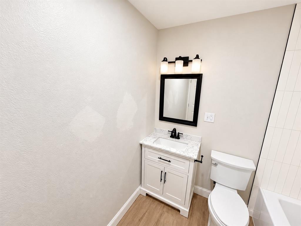 Vanity featuring a stone-look countertop, integrated rectangular sink, matte black faucet, shaker-style cabinetry, and three-light wall-mounted fixture